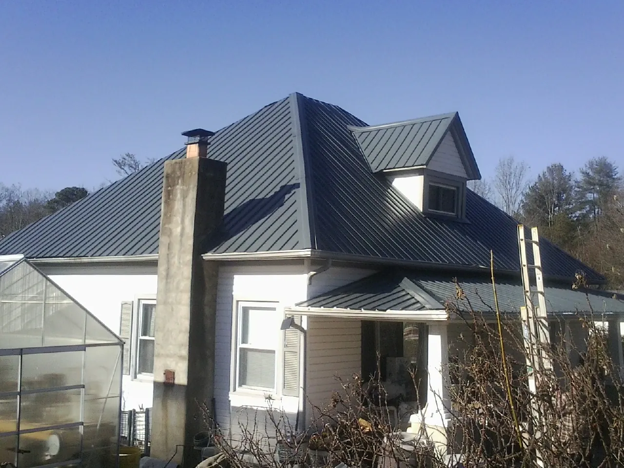 Dark blue standing seam metal roof on a white farmhouse with dormer — Slate & Tile Roof Repair by Roofing Brothers in Barboursville