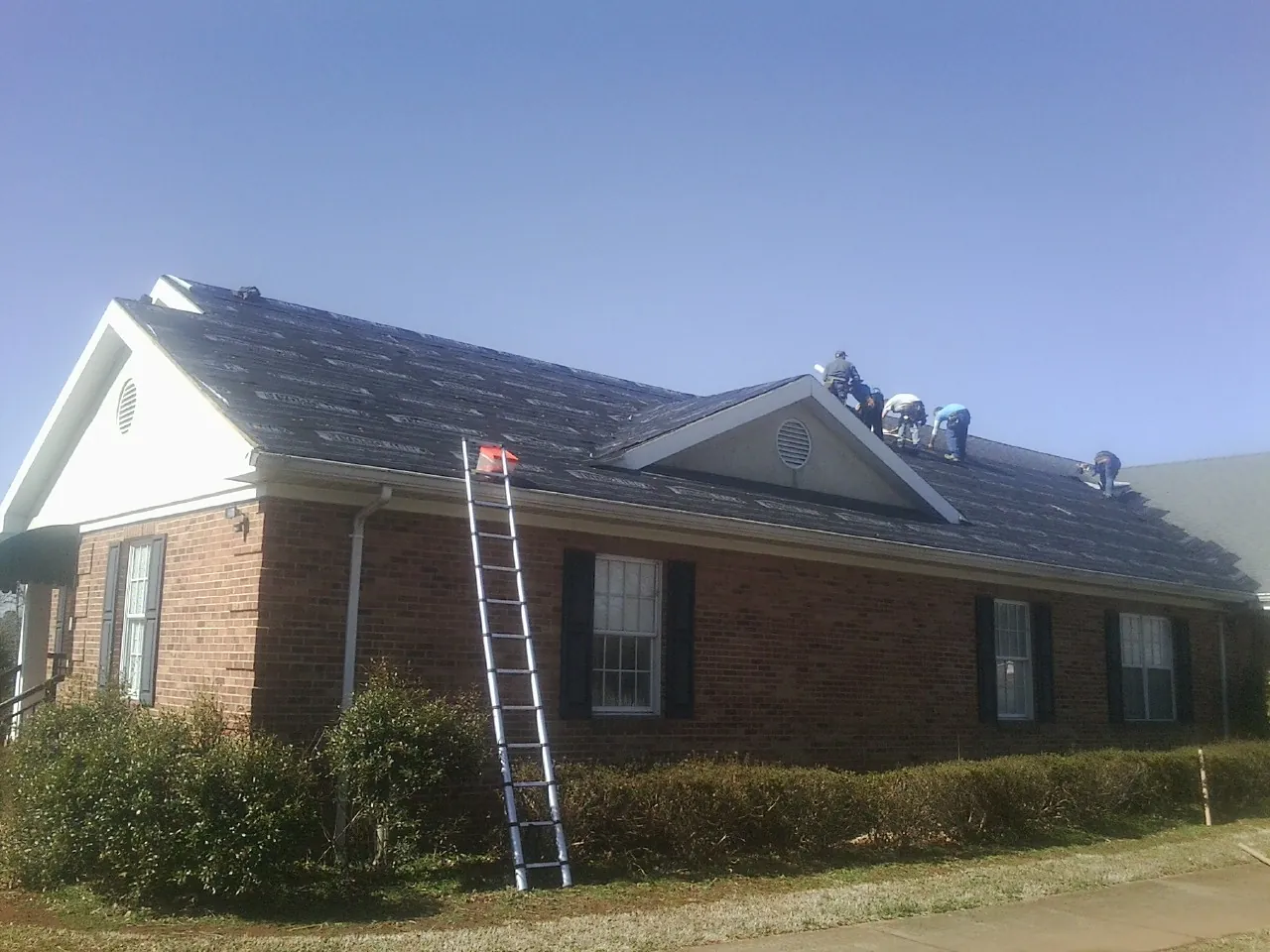 Crew tearing shingles off a brick ranch roof with a ladder set — Emergency Roof Repair work by our crew in Barboursville