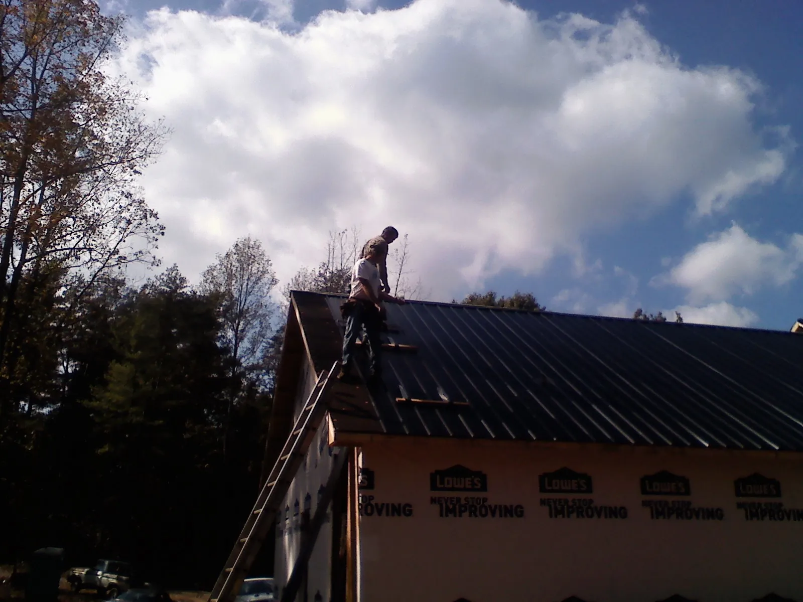 Roofer fastening dark metal panels high against a cloudy sky, from a Roof Inspection job in Barboursville