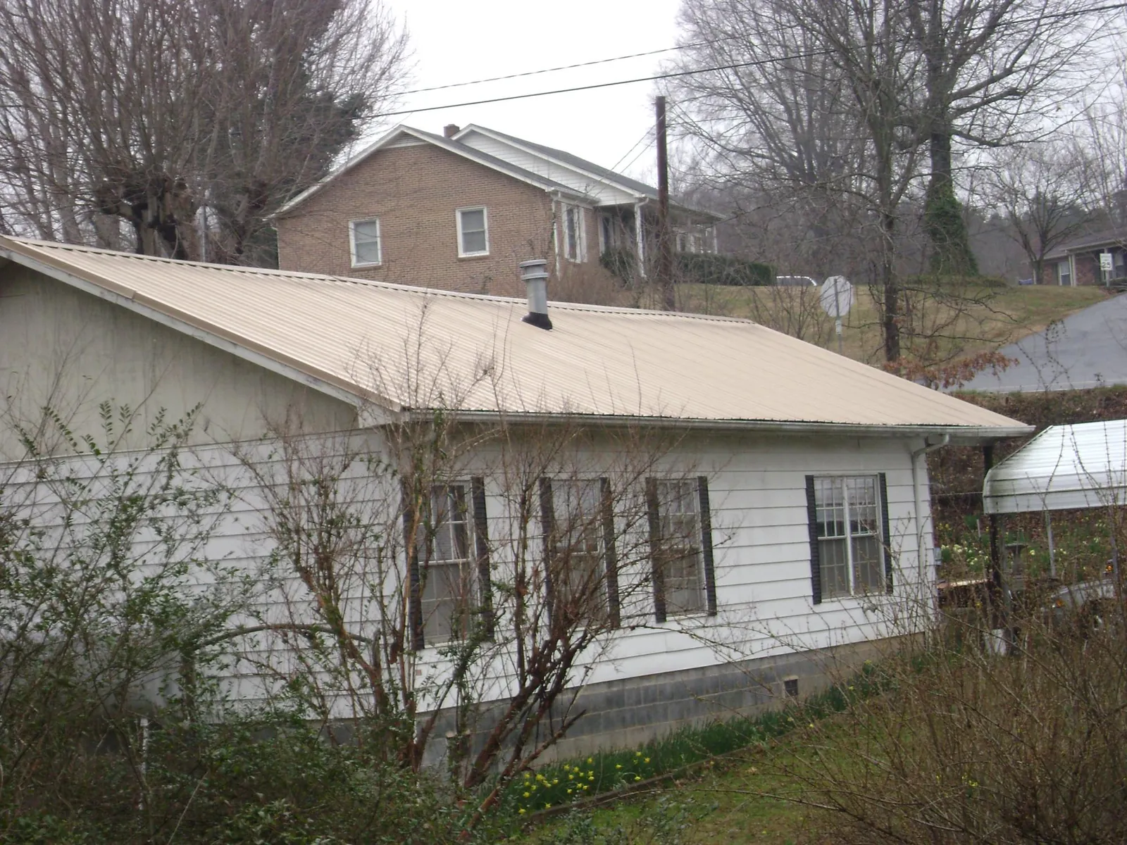 Tan metal roof on a white sided house set into a hillside — Commercial Roofing by Roofing Brothers in Barboursville